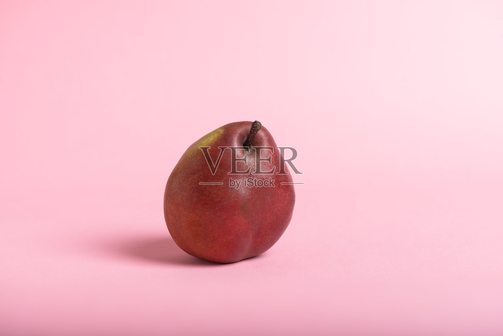 一只成熟的红色梨子静静地放在淡粉色的背景上。照片摄影图片