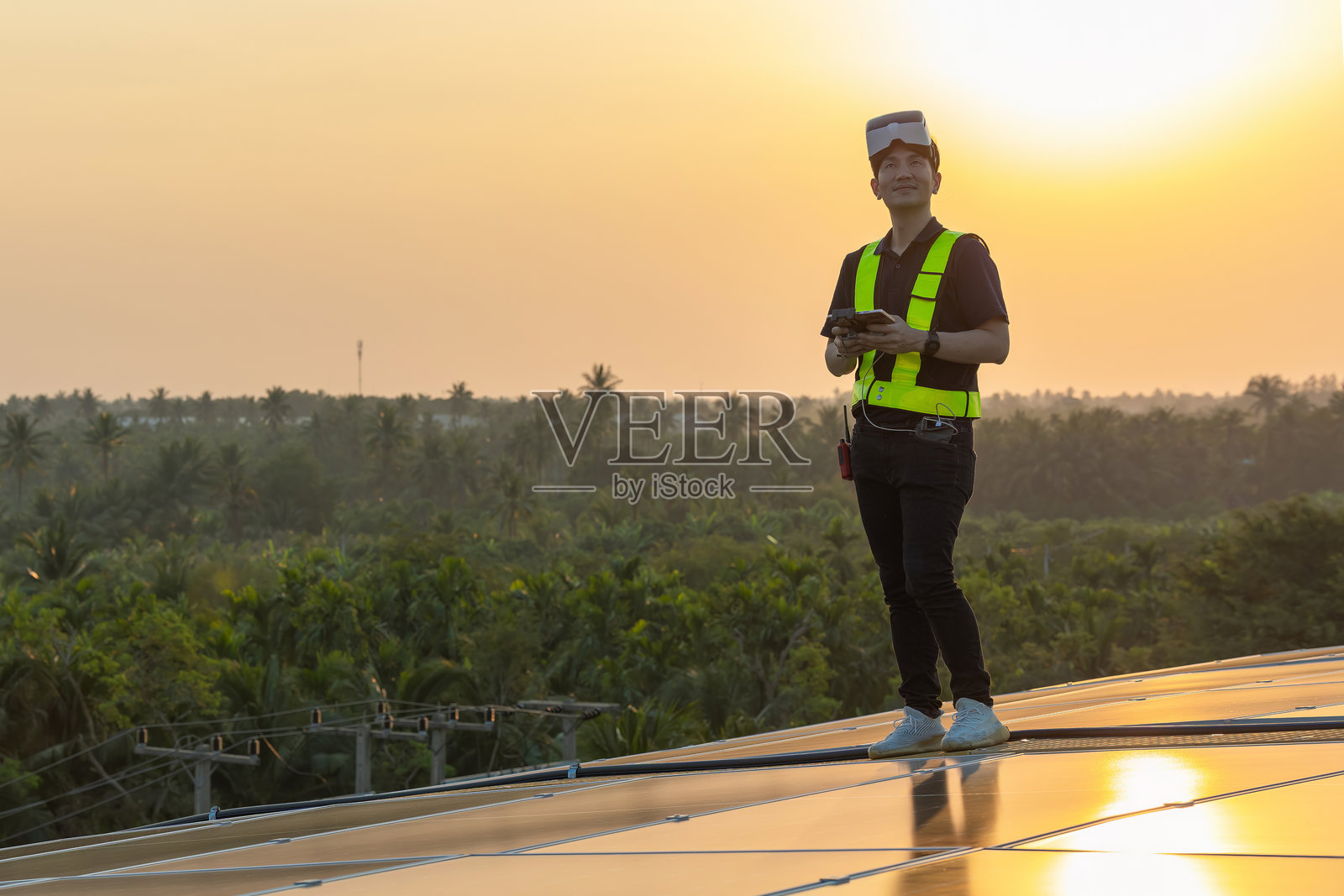 技术太阳能电池工程师服务检查工厂屋顶太阳能电池的安装。工程师操控无人机从上方检查工厂屋顶太阳能面板的安装情况，背景是日落。照片摄影图片