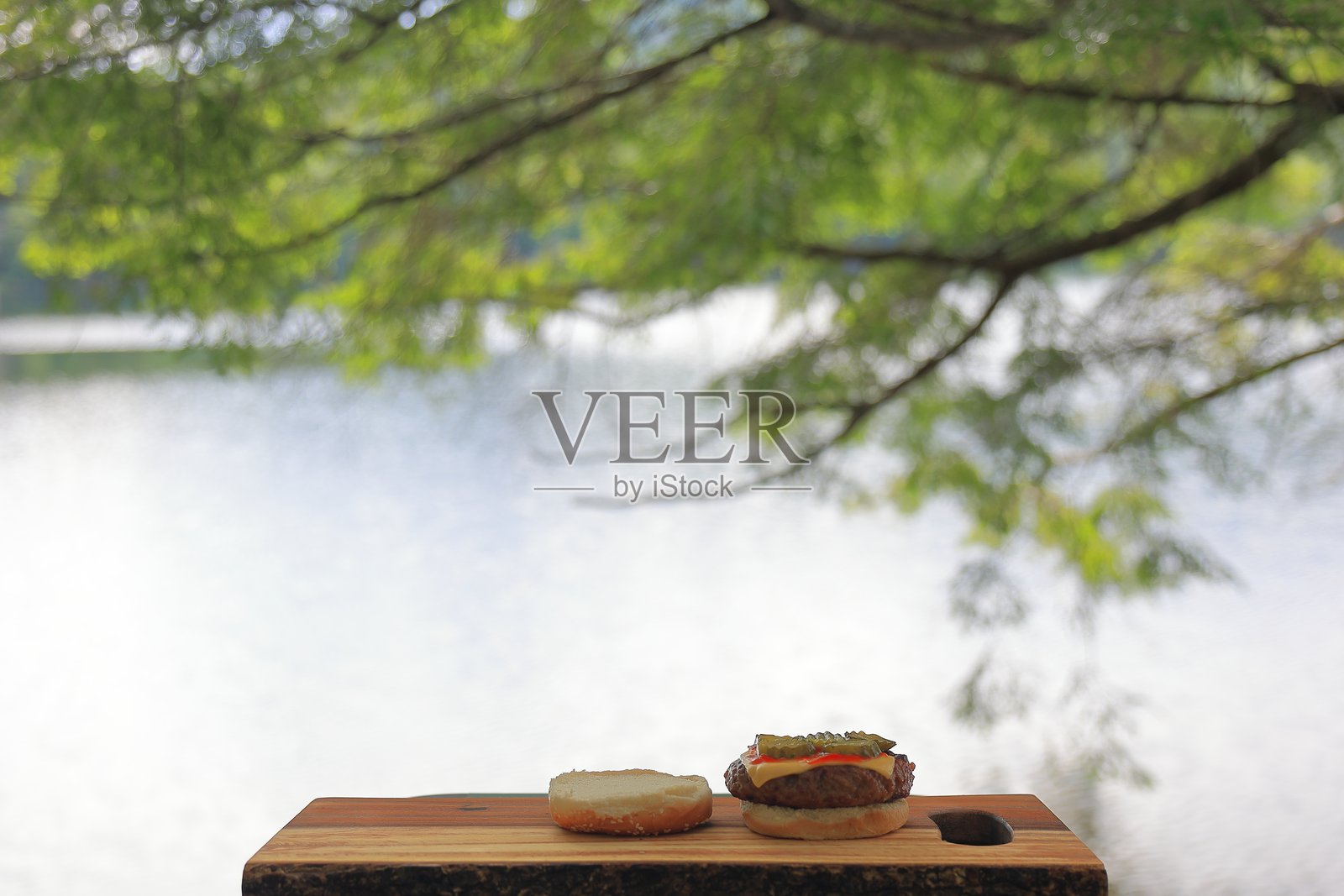 开放式芝麻种子汉堡放在木砧板上，位于风景如画的湖边照片摄影图片