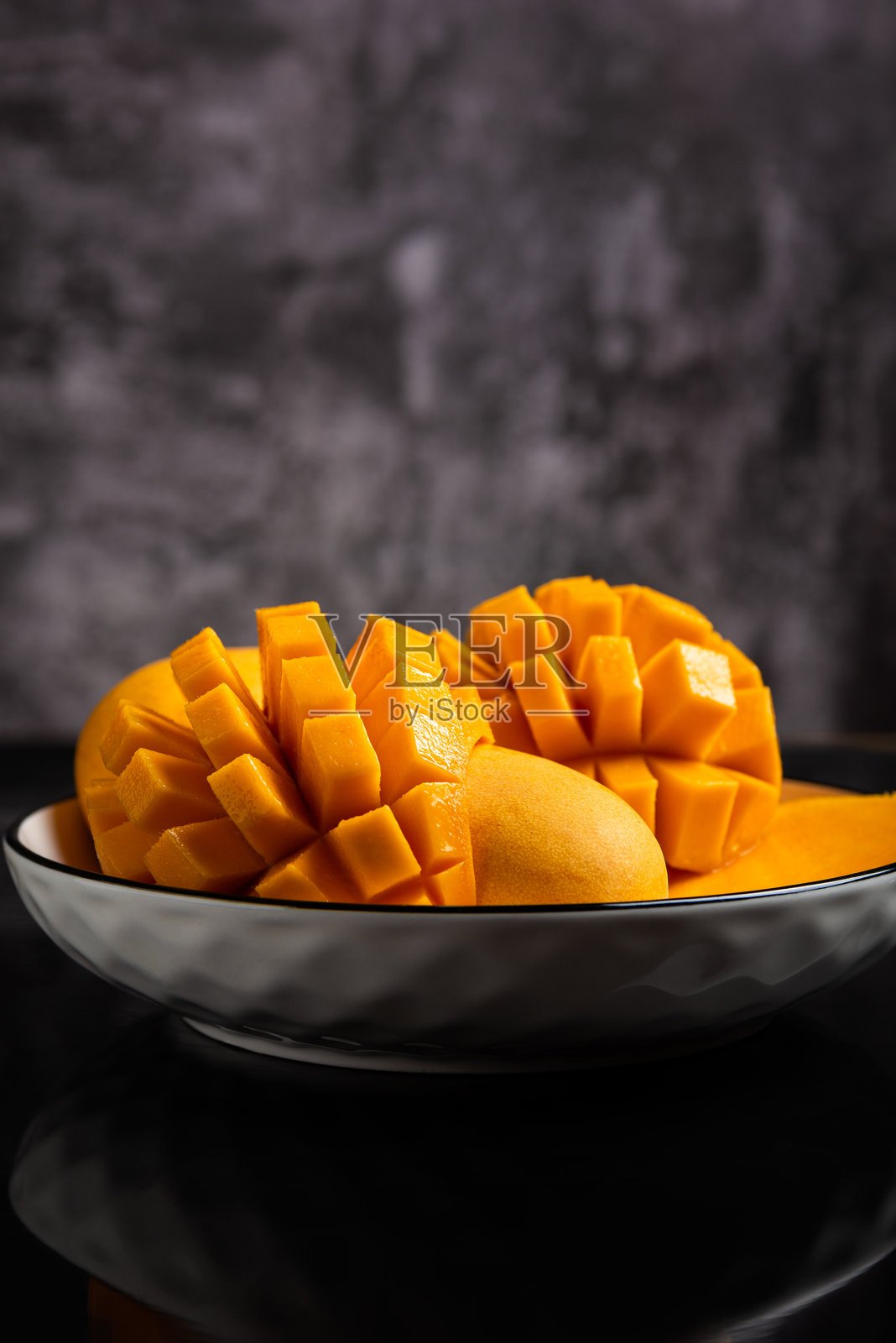 一个白色碗里盛着鲜艳的黄色芒果，有些切成完美的方块，有些则是整颗的。照片摄影图片