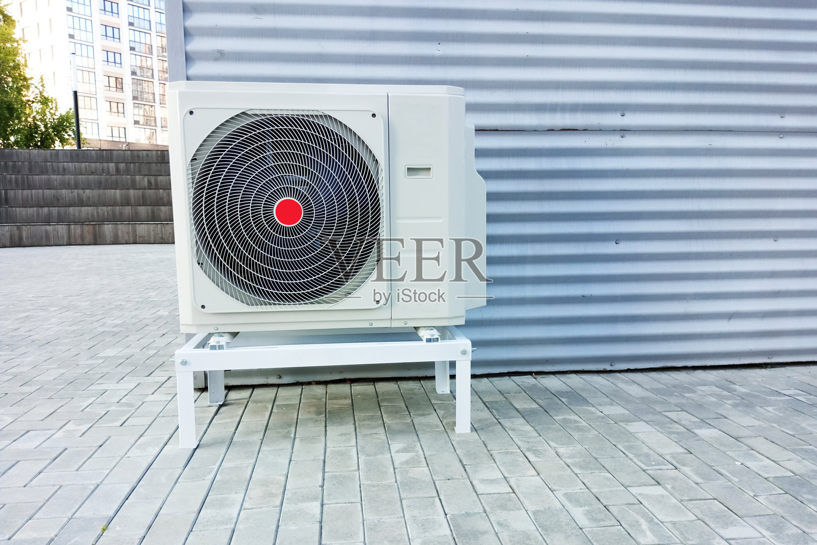 建筑墙壁旁的金属支架上的户外空调机组。照片摄影图片