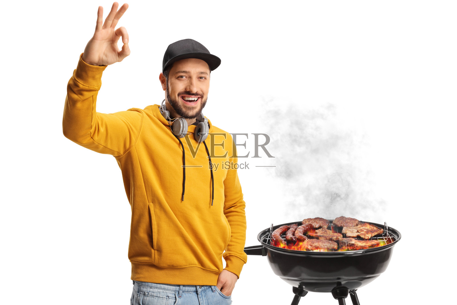 年轻男子戴着耳机，在烧烤前做出“好的”手势照片摄影图片
