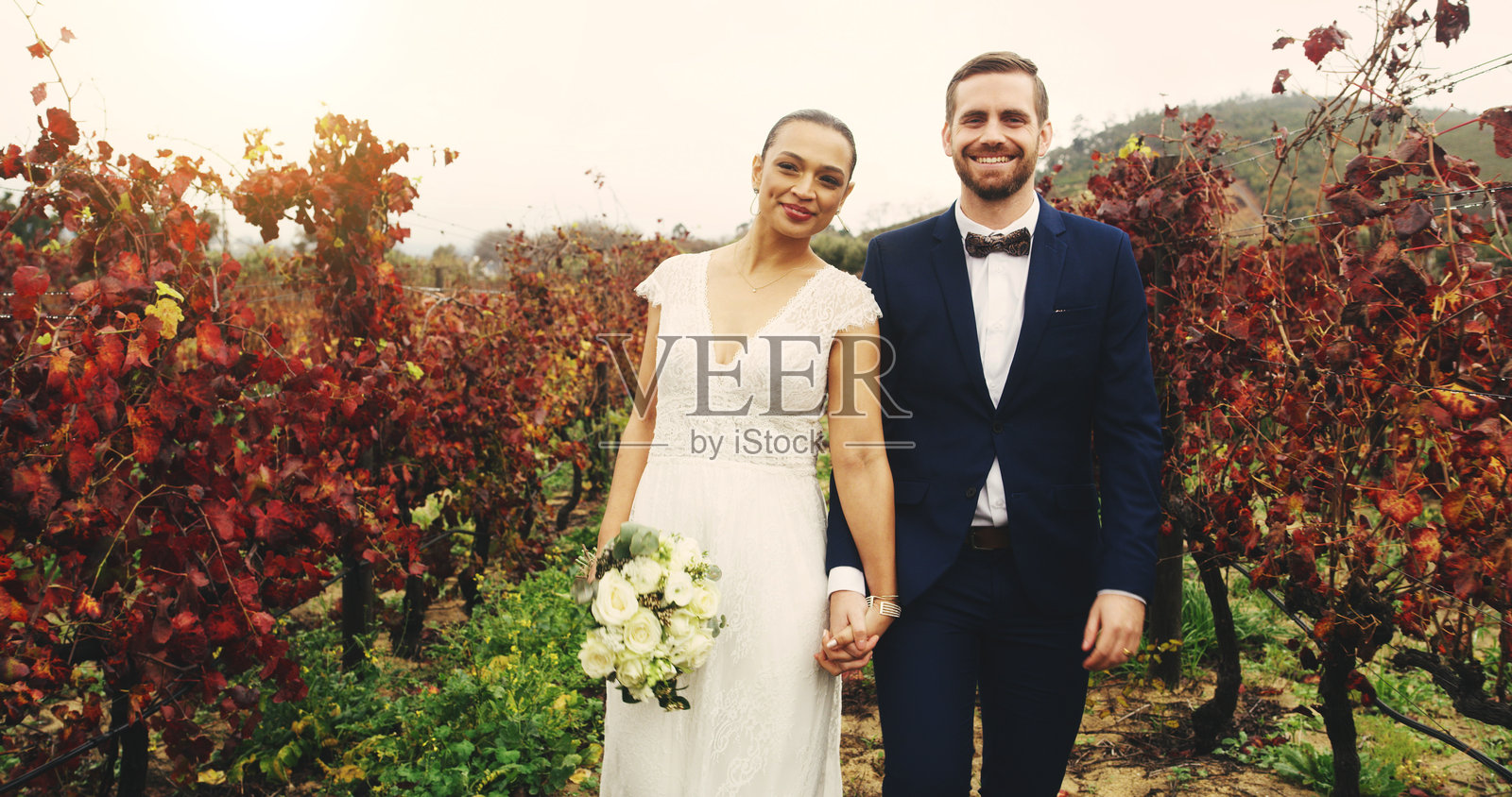 在葡萄园中，手牵手的情侣肖像，庆祝或活动的婚礼。户外的已婚夫妇展现出承诺、爱与微笑，适合婚礼、婚姻或里程碑的场合。照片摄影图片