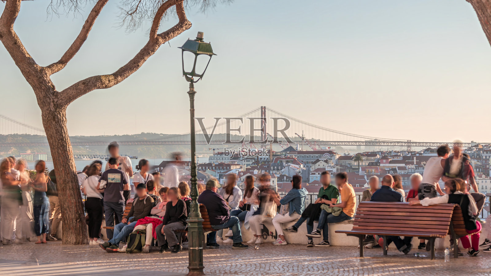 人们在葡萄牙里斯本的格拉萨观景台观看日落时的25号桥城市全景延时摄影照片摄影图片