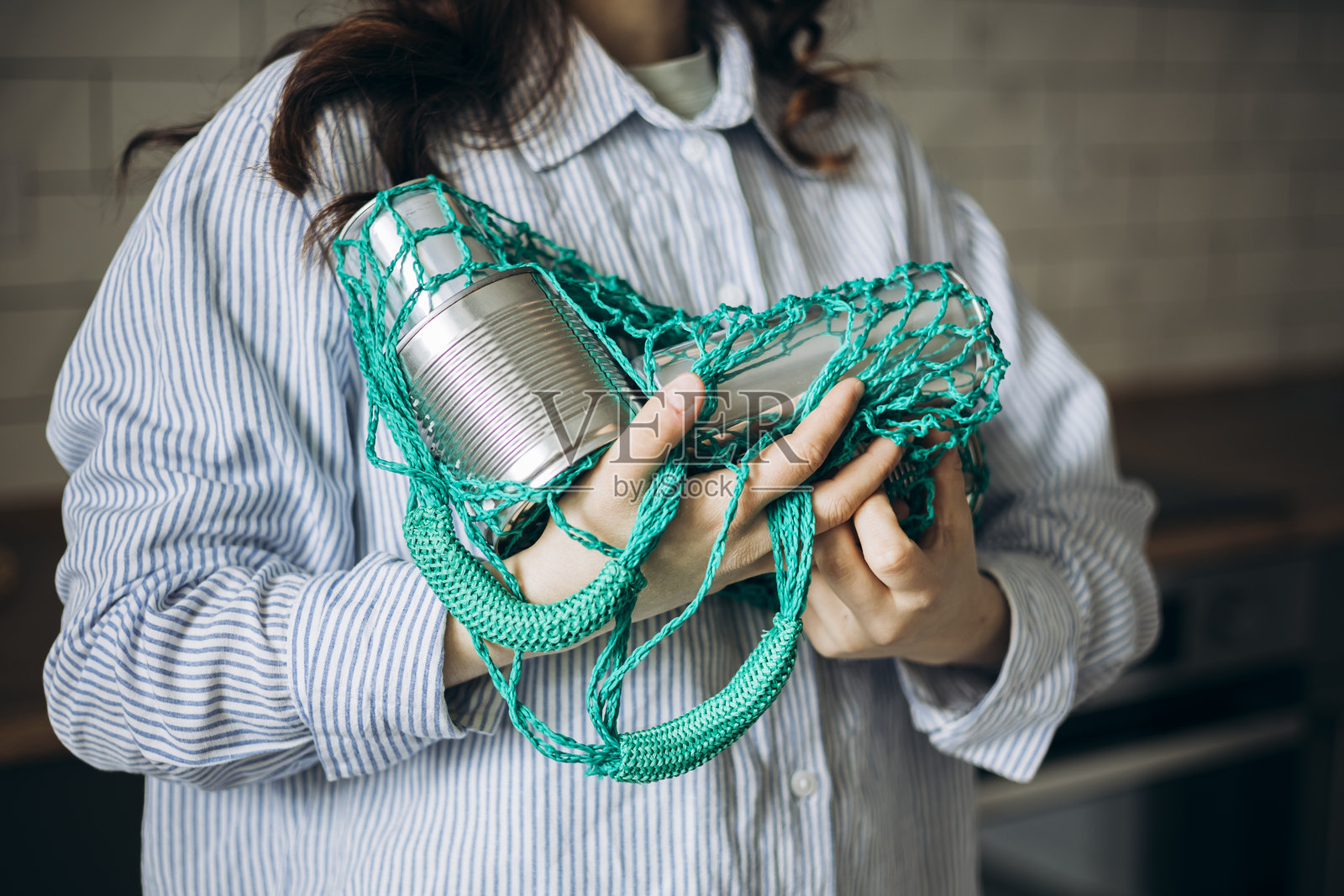 女人在厨房里拿着一个装有空罐头的网袋，在家进行回收。照片摄影图片