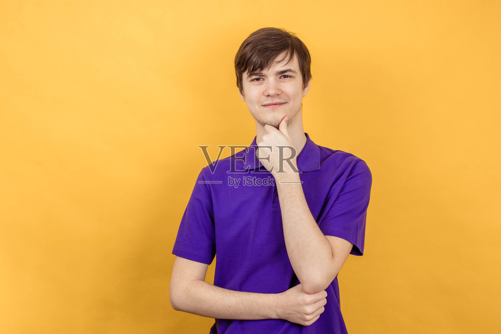 年轻男子的特写肖像，背景为黄色，手托着脸庞，注视着镜头。照片摄影图片