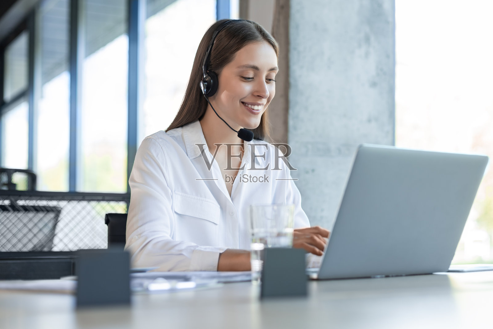 友好的女性热线接线员在呼叫中心。年轻女性在呼叫中心工作，手中握着耳机麦克风。照片摄影图片