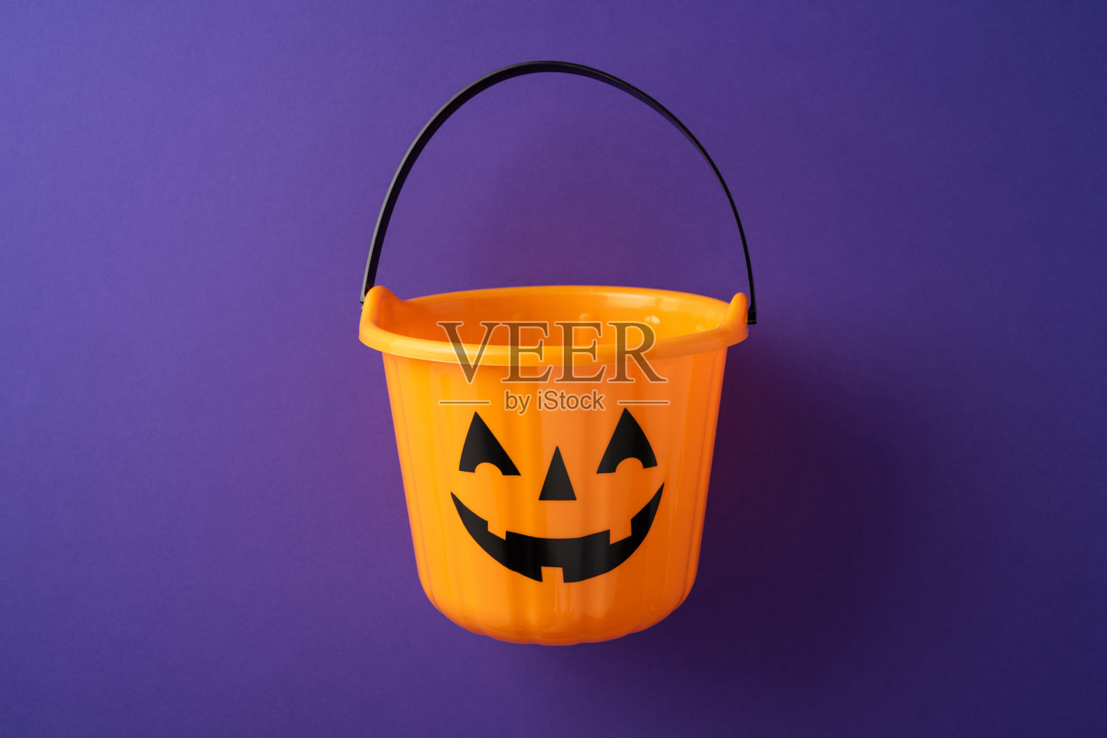 装饰性橙色南瓜桶，带有微笑的面孔，背景为节日紫色。照片摄影图片
