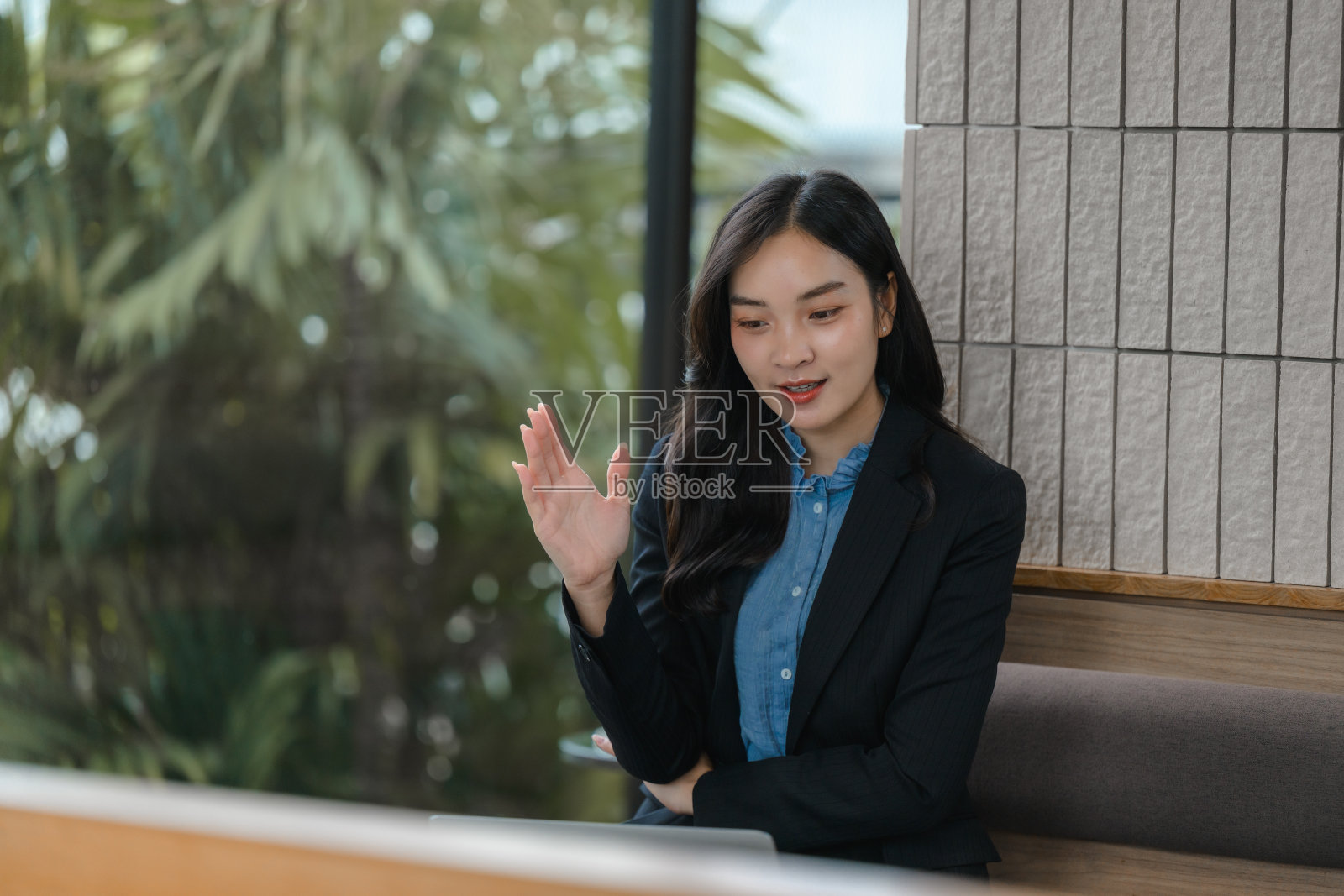 年轻的亚洲女商人在时尚现代的办公室里，微笑着挥手与笔记本电脑上的视频通话。办公室充满自然光。照片摄影图片