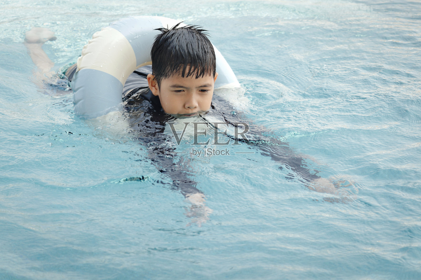快乐的亚洲男孩在蓝色水面上漂浮着游泳圈。放松的孩子在夏季假期的户外游泳池中玩充气圈。快乐的孩子在周末的泳池中游泳。照片摄影图片