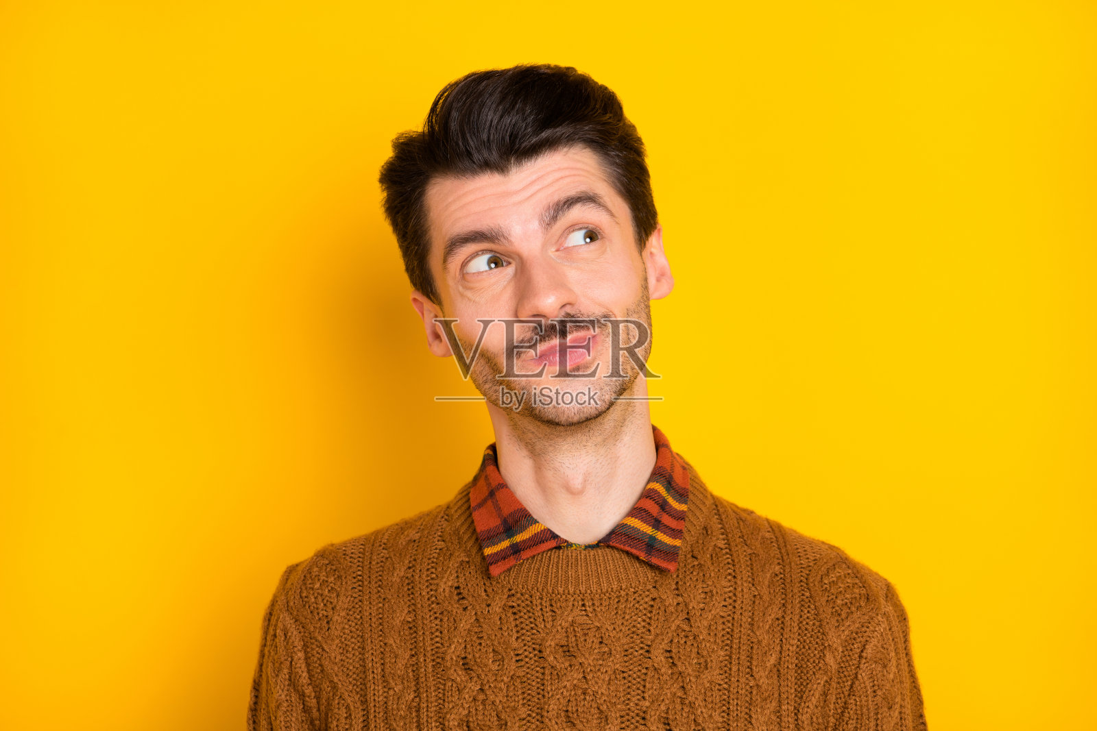 好奇的年轻胡子男士穿着棕色毛衣，凝视空旷的空间，背景为鲜艳的黄色。照片摄影图片