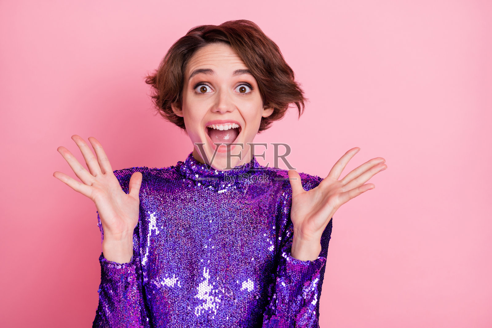 惊讶的女孩穿着紫色奢华裙子，张嘴凝视，双手做出手势，背景为柔和的粉色。照片摄影图片