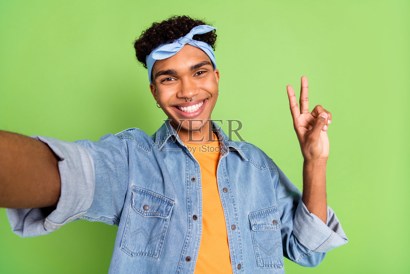 乐观的棕发男孩在绿色背景下穿着蓝色衬衫，做出V字手势自拍。照片摄影图片