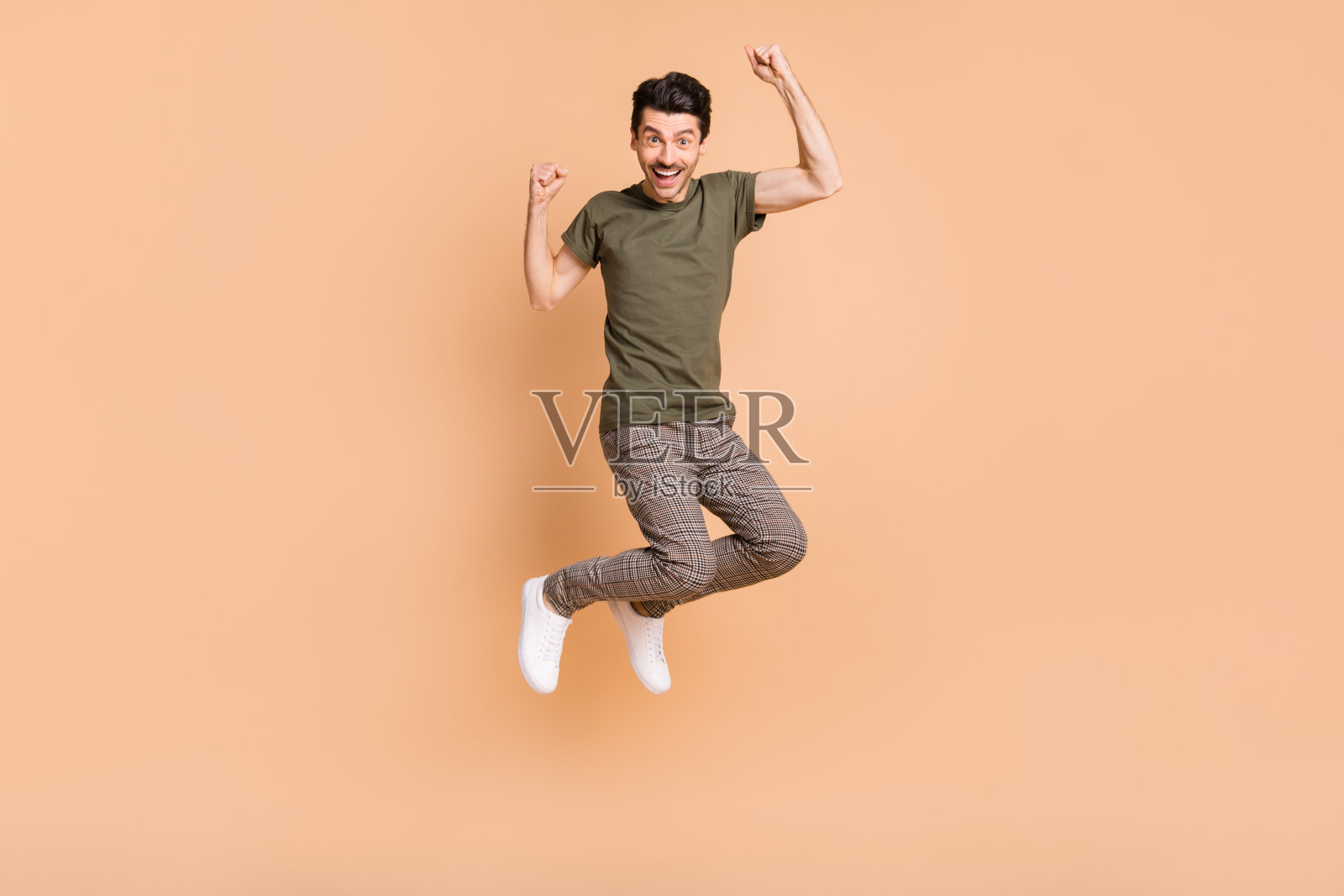 高兴地跳跃的男士全身照，像胜利者一样做出手势，背景为柔和的米色。照片摄影图片
