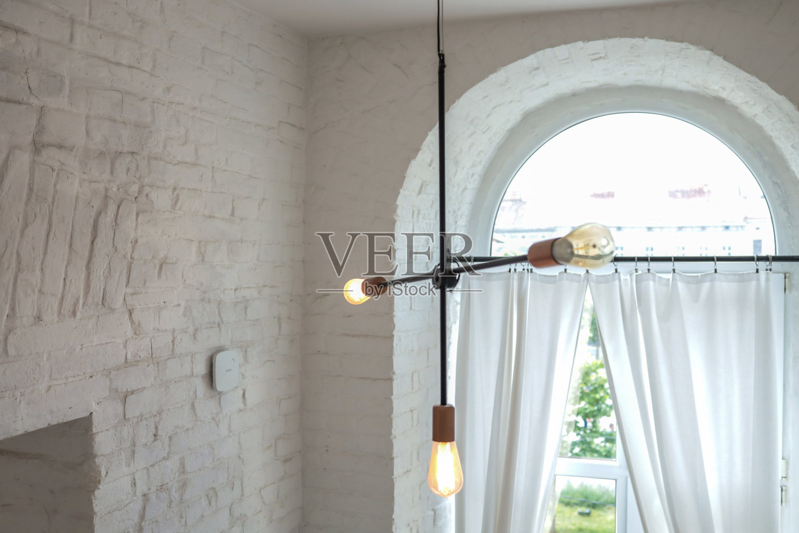 极简主义的阁楼室内，配有工业风吊灯和大型拱形窗户。白色砖墙和柔软的窗帘营造出明亮、通透的氛围。照片摄影图片