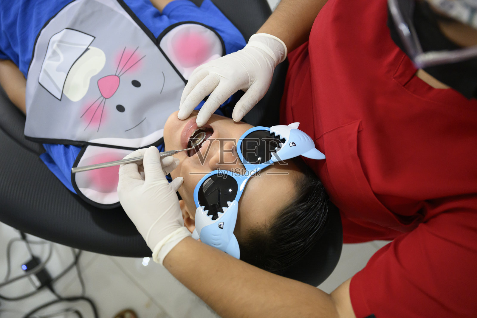 牙医在进行牙科检查时为佩戴保护眼镜的儿童患者检查牙齿照片摄影图片