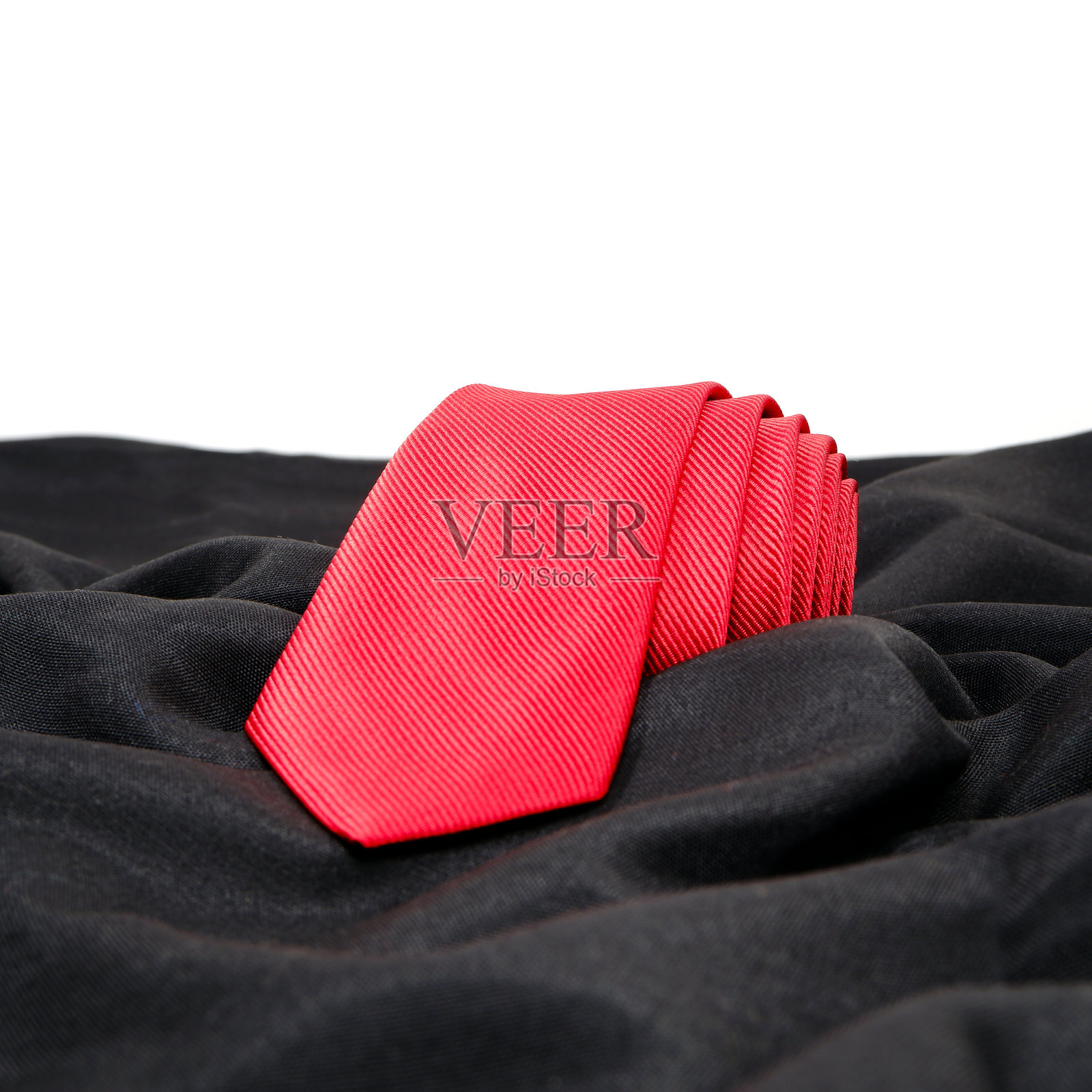 红色领带卷在黑色布料上，白色背景的特写视图照片摄影图片