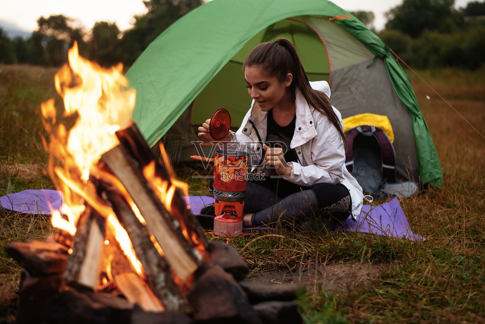 微笑的年轻女性正在把水壶放在火上照片摄影图片