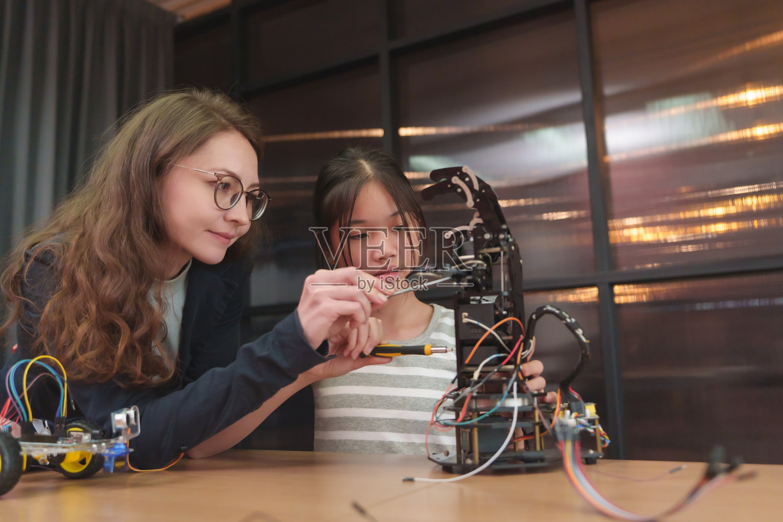 老师帮助亚洲女孩学生进行团队合作，构建机器人手臂和STEM实践活动。照片摄影图片