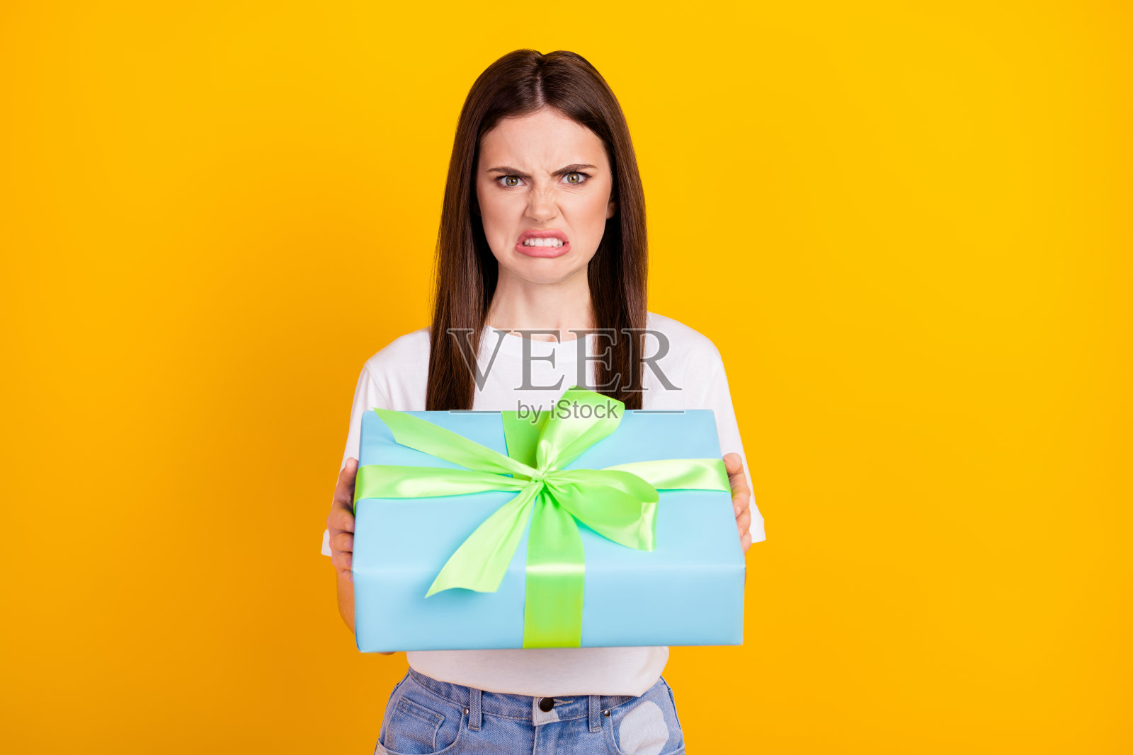 收到生日礼物感到失望和厌恶的女孩，情绪低落，孤立在黄色背景上。照片摄影图片