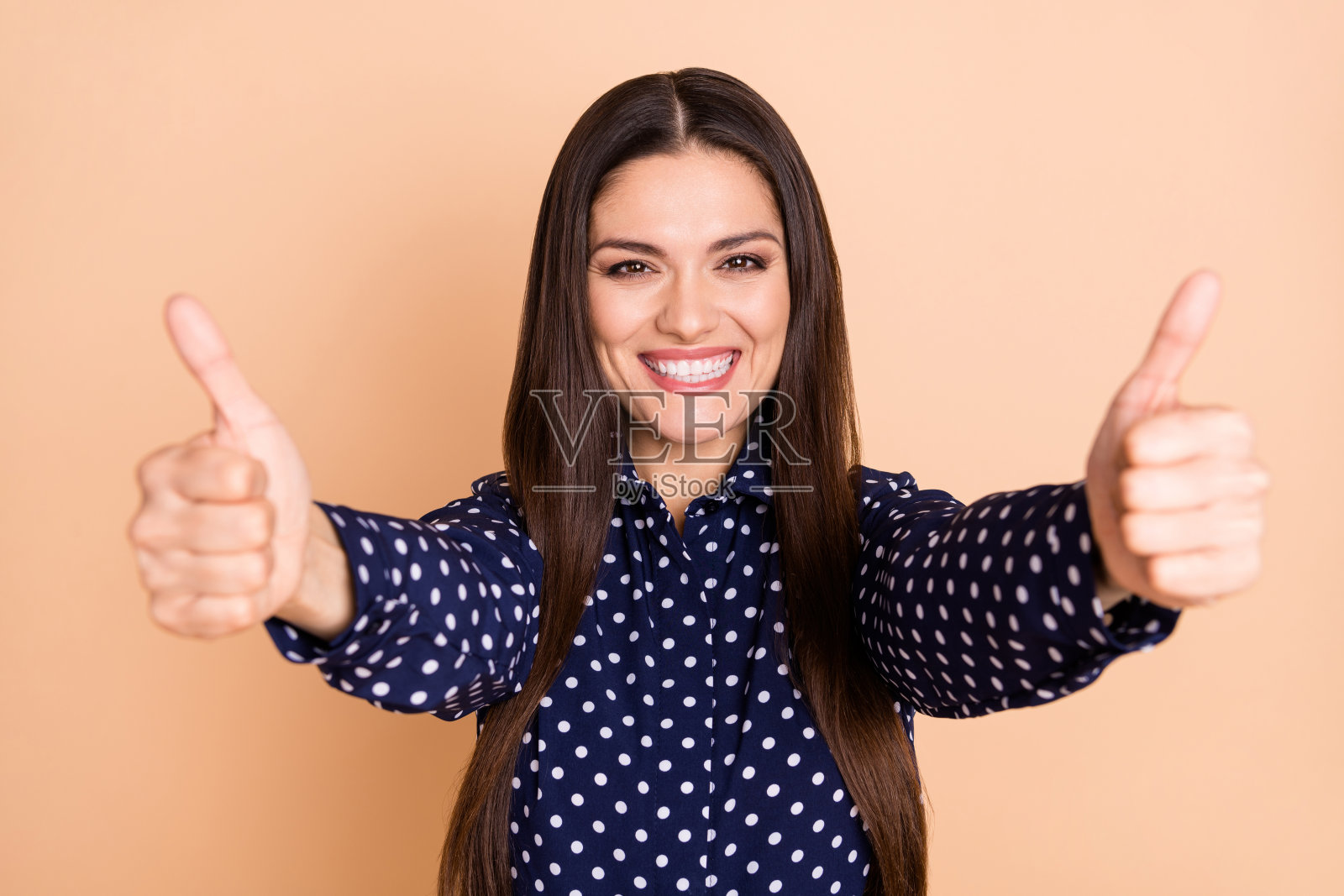 积极美丽的人物，双手竖起大拇指，露出灿烂的微笑，背景为米色。照片摄影图片