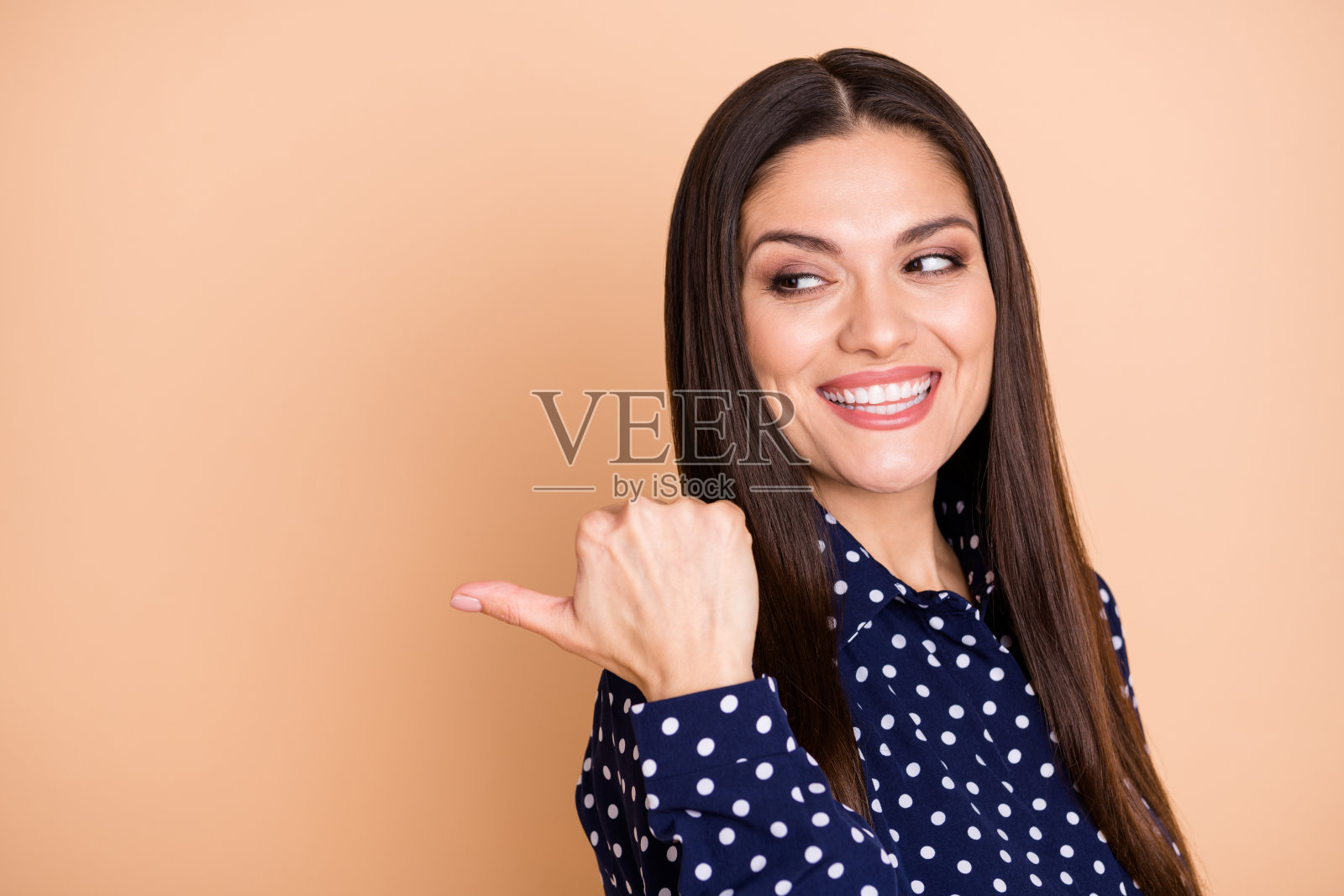 愉快迷人的人指着空白区域，表现出兴趣，背景为米色。照片摄影图片