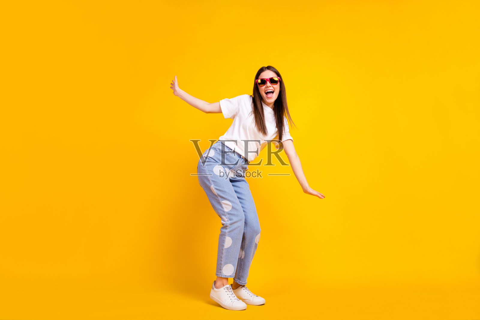 年轻女孩全身侧面照，兴奋快乐，面带微笑，顽皮有趣，背景为黄色。照片摄影图片