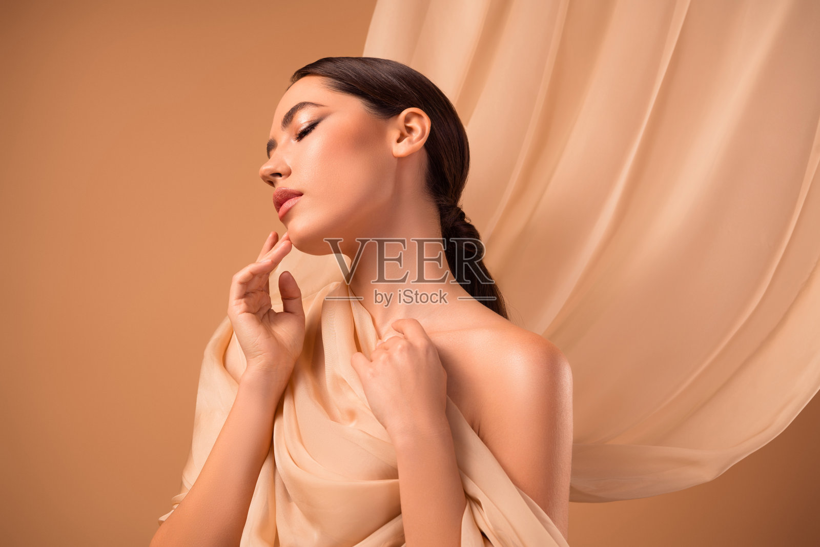 年轻的棕发女性在米色背景下以时尚姿势展现美丽与护肤。照片摄影图片