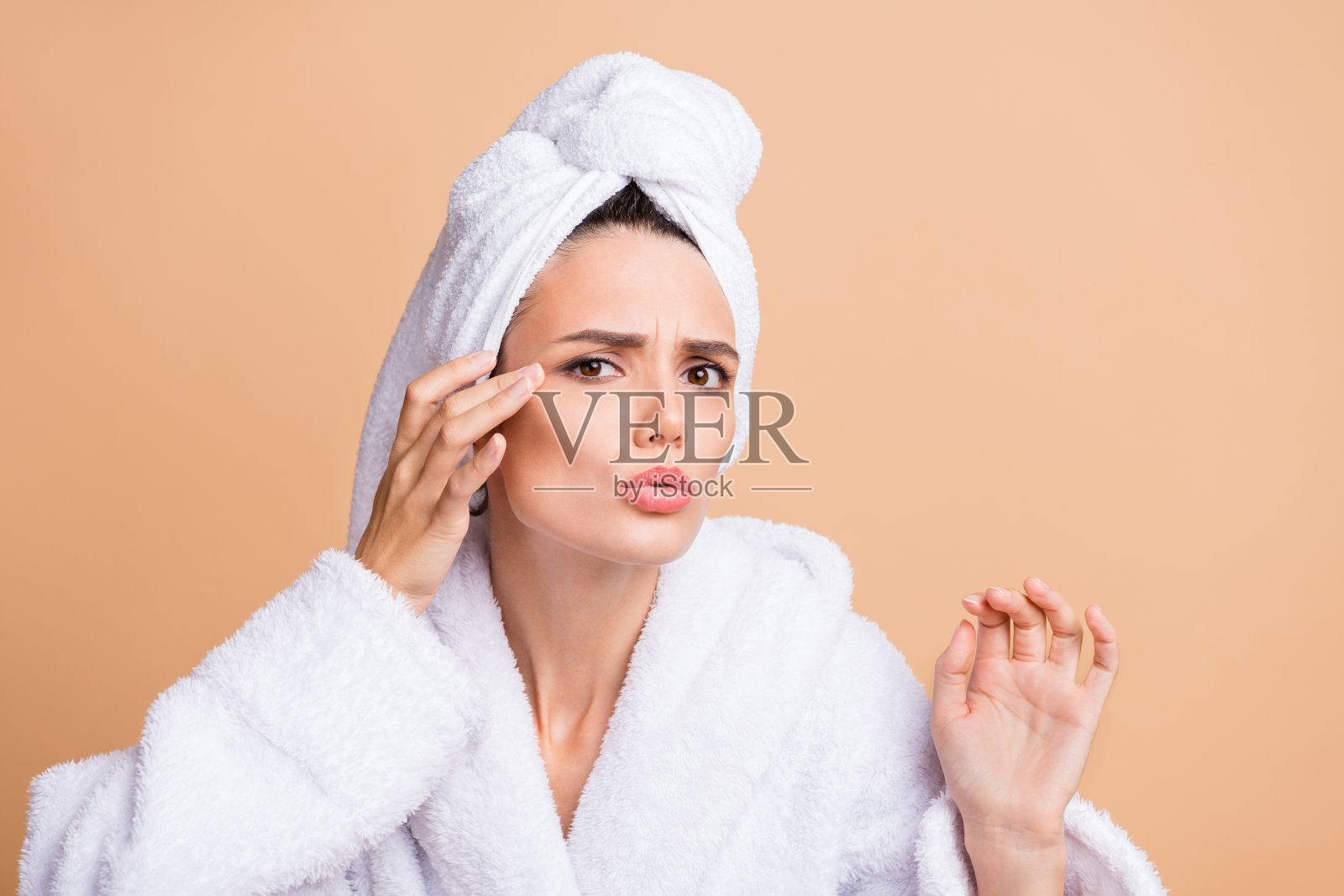 穿着浴袍的漂亮忧虑梦幻女孩，触摸敏感肌肤上的黑色斑点，背景为米色柔和色调。照片摄影图片