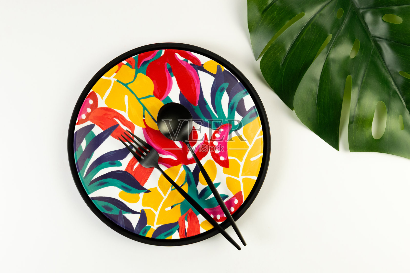 黑色托盘上方视角，五彩盘子，黑色餐具，背景为白色。异国植物盘，龟背竹叶，夏季野餐。照片摄影图片