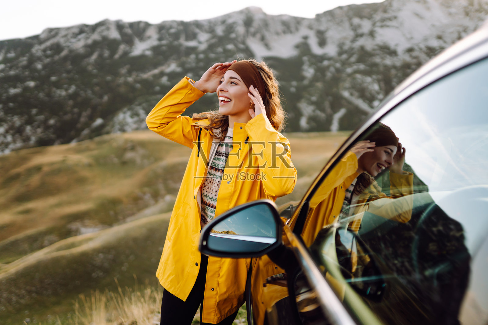 穿着亮色雨衣的旅行者坐在汽车后备厢中，欣赏山景。照片摄影图片