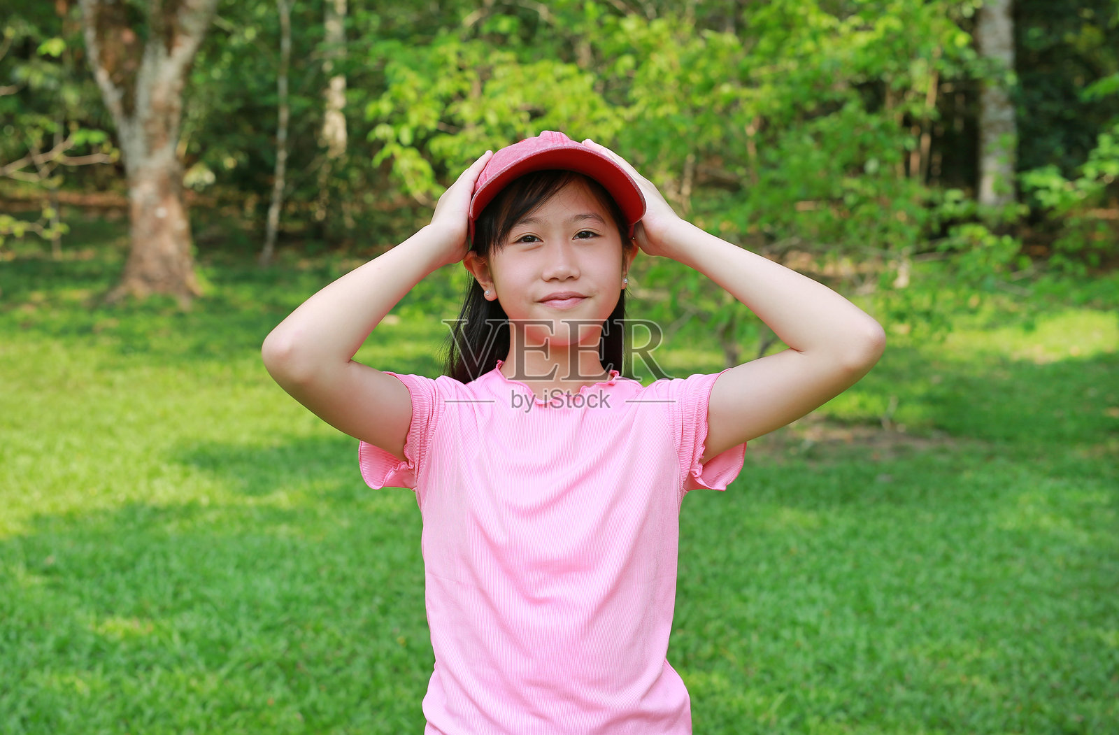 亚洲女孩穿着粉色帽子，手握帽子，直视镜头，站在花园里。特写镜头。照片摄影图片