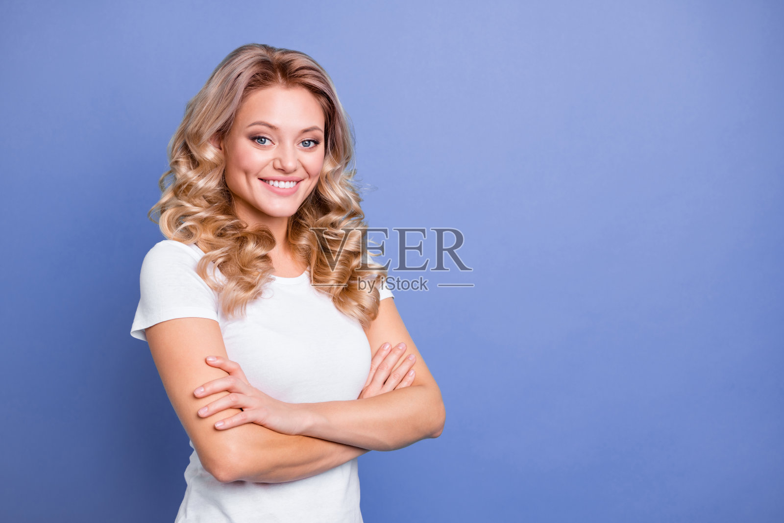 年轻迷人、快乐积极、微笑的女商人双手交叉，背景为蓝色。照片摄影图片