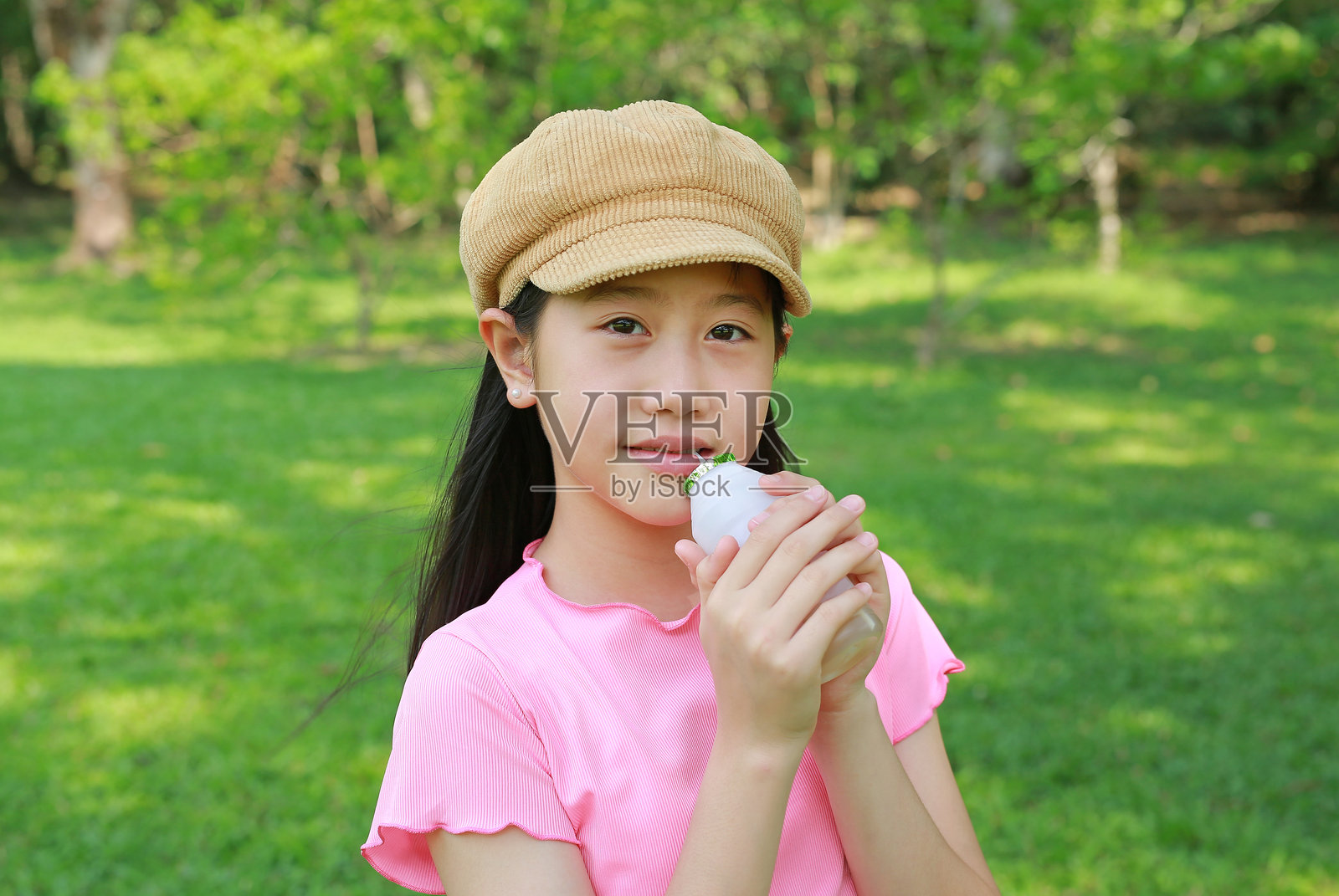 亚洲女孩在花园里通过吸管喝牛奶饮料。照片摄影图片