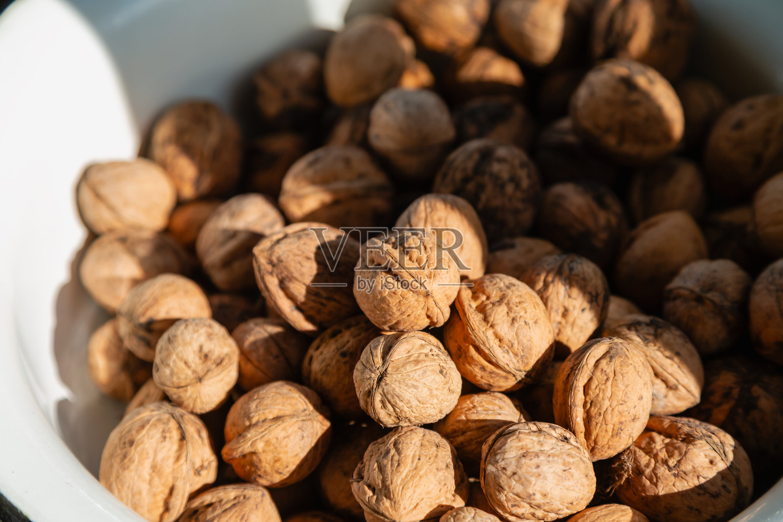 温暖阳光下的核桃，静静躺在白色盘子上，特写镜头，光影中的核桃，核桃收获。照片摄影图片