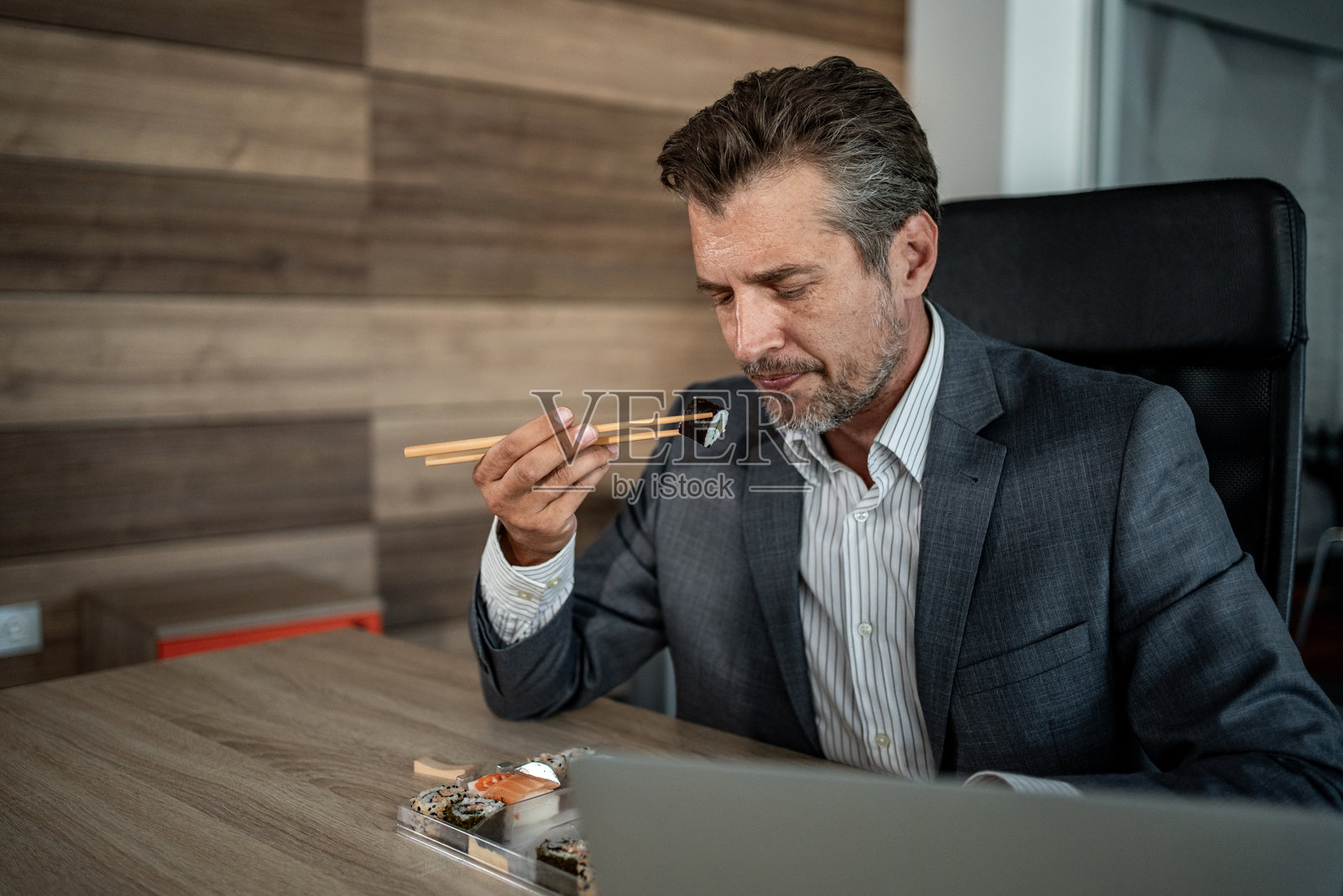 商人在办公室一边吃寿司一边使用笔记本电脑工作照片摄影图片