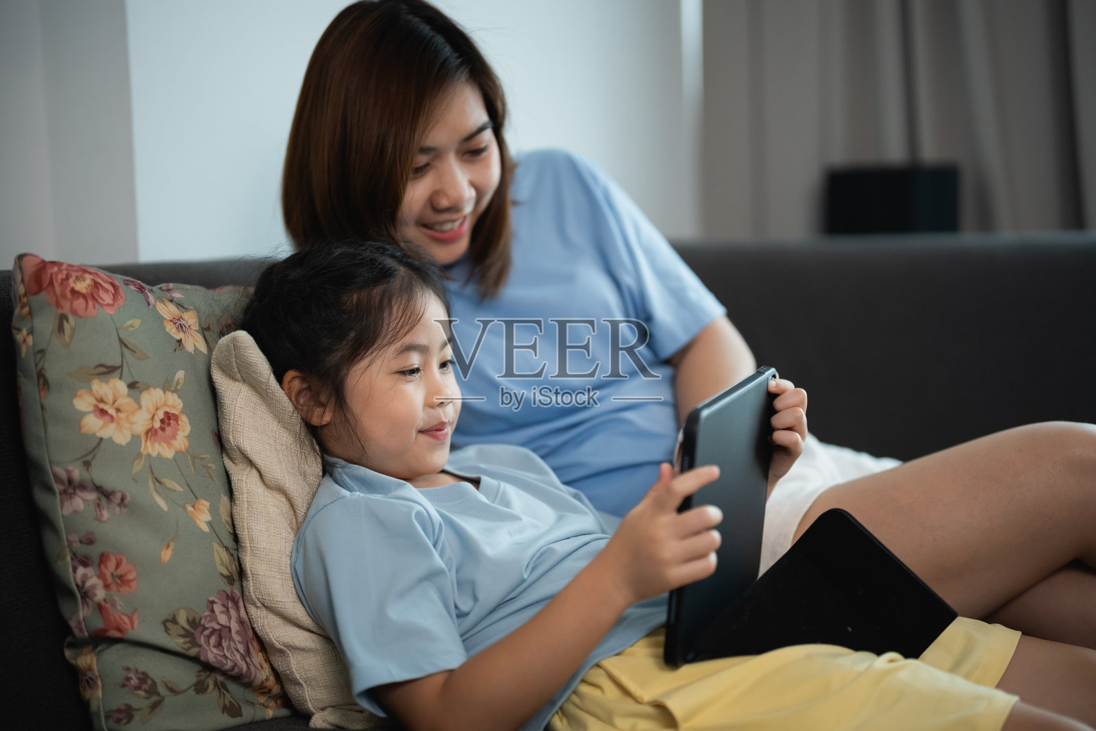 享受美好时光：母女在舒适的客厅沙发上互动使用平板电脑照片摄影图片