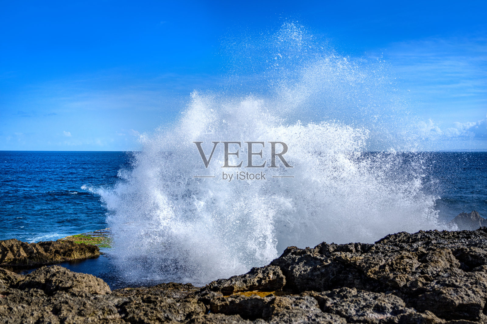 阳光明媚的日子里，波涛拍打着岩石海岸照片摄影图片