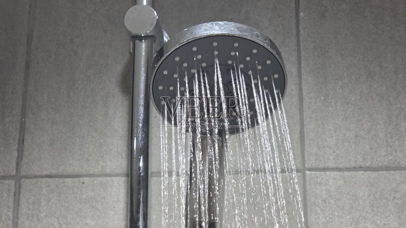 现代铬制淋浴头喷出直流水流，安装在瓷砖墙上，展示室内管道和沐浴设施照片摄影图片