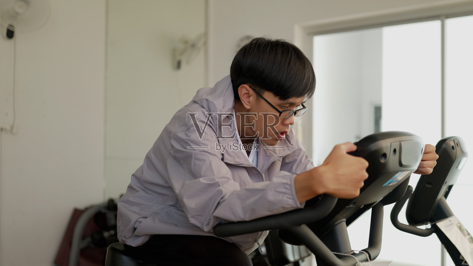 健身房骑行课程，配有平板娱乐——亚洲男性平衡健康与休闲。4K照片摄影图片