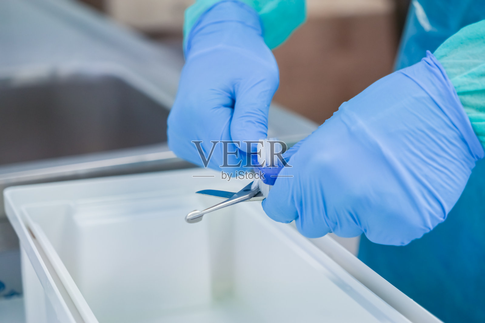 医疗专业人员戴着蓝色手套，细致地用刷子清洁手术器械，确保为患者安全和感染控制进行消毒。照片摄影图片