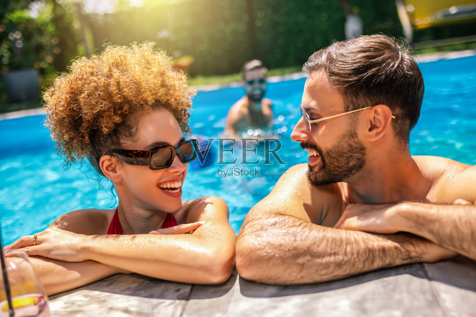 阳光明媚的夏日，快乐的朋友们在泳池旁放松。照片摄影图片