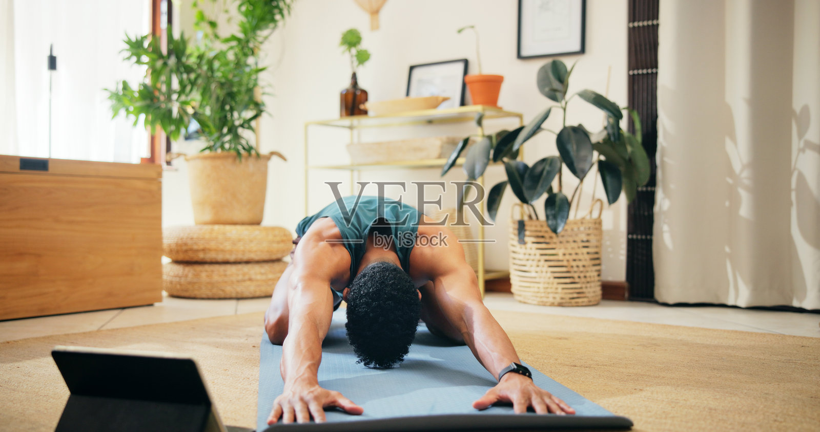 男子在家中瑜伽垫上使用平板电脑进行拉伸，以缓解肌肉紧张，早晨锻炼和在线课程。健身、普拉提和在地板上观看视频教程的个人进行婴儿式姿势和锻炼。照片摄影图片