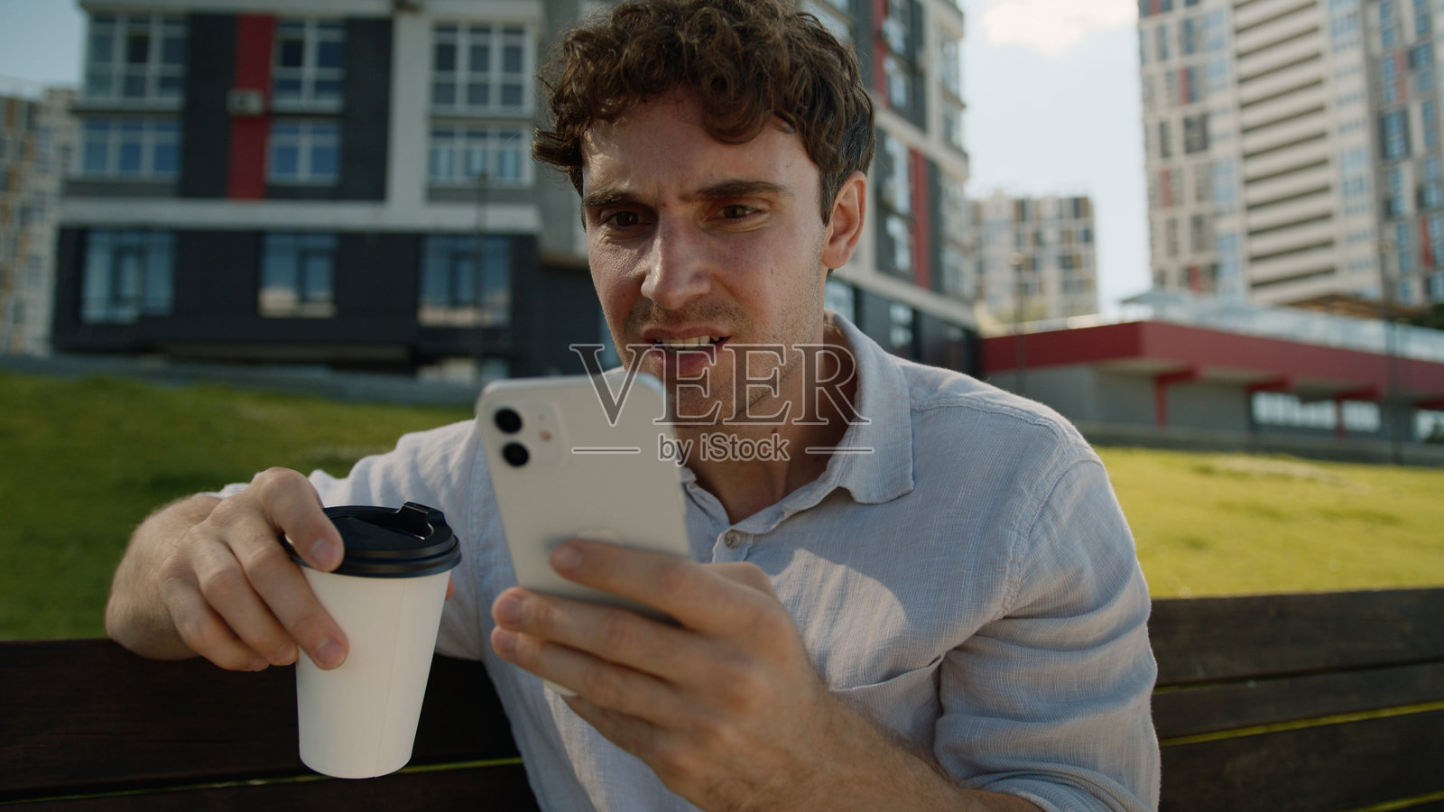 白人男性在户外喝咖啡，手里拿着手机，因在线赌博失败而感到沮丧和压力。照片摄影图片