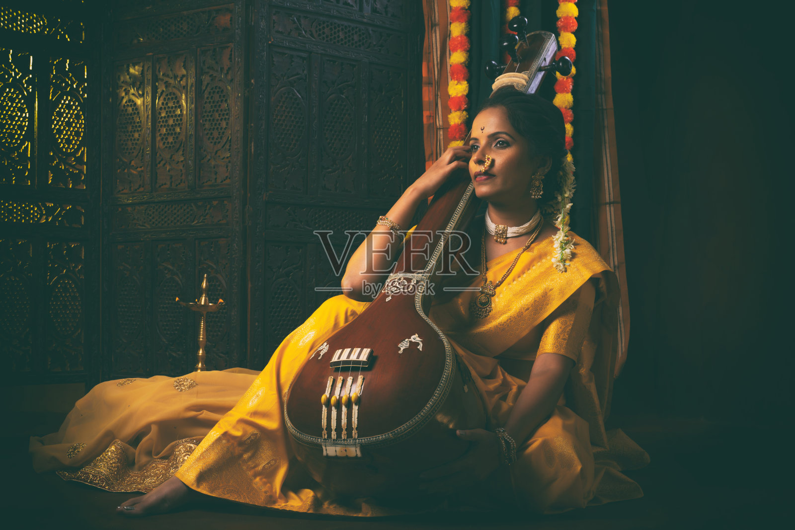 身穿黄色纱丽的年轻印度女性手持一种名为坦普拉或坦博拉的乐器，正沉浸在音乐的氛围中。照片摄影图片