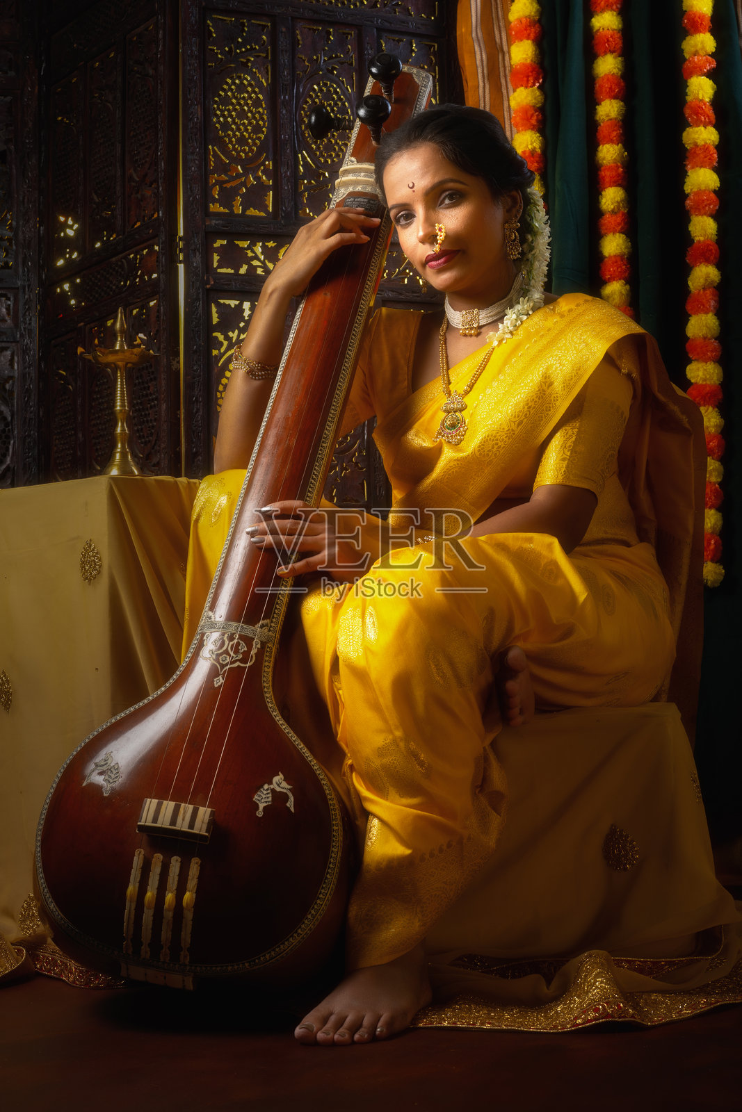 年轻的印度女性穿着黄色纱丽，手持一种名为坦普拉或坦博拉的乐器，正沉浸在音乐的氛围中。照片摄影图片