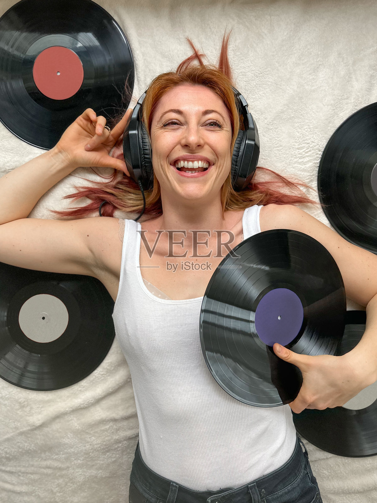 30多岁的女性，穿着舒适的家居服，躺在床上，戴着耳机听音乐。周围是复古的黑胶唱片。照片摄影图片