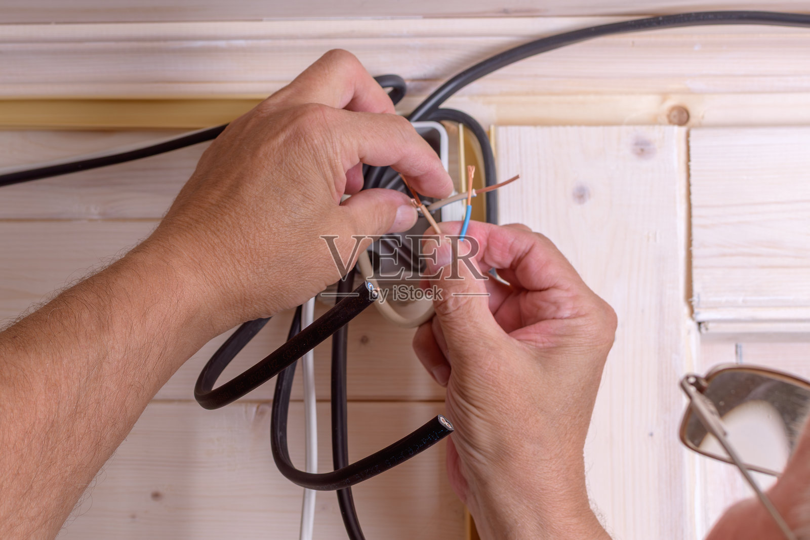电工用手将铜线扭在一起，为浅色木墙上的接线盒准备可靠的电气连接。照片摄影图片