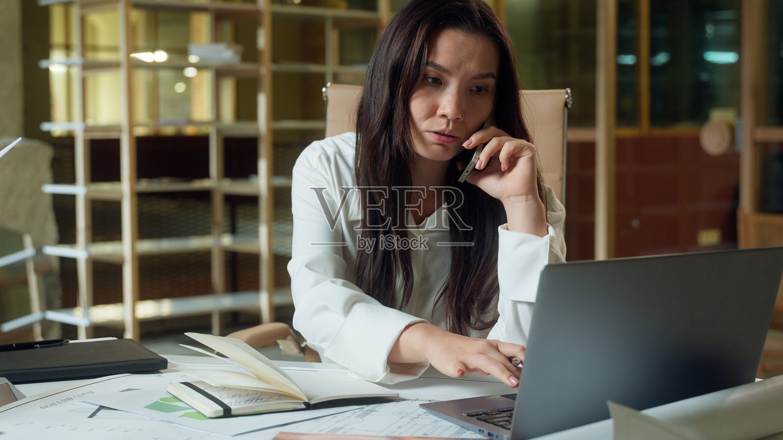 亚洲女商人，使用手机与客户在线咨询，办公桌前的女性商务人士，正在笔记本上写下任务和笔记。照片摄影图片