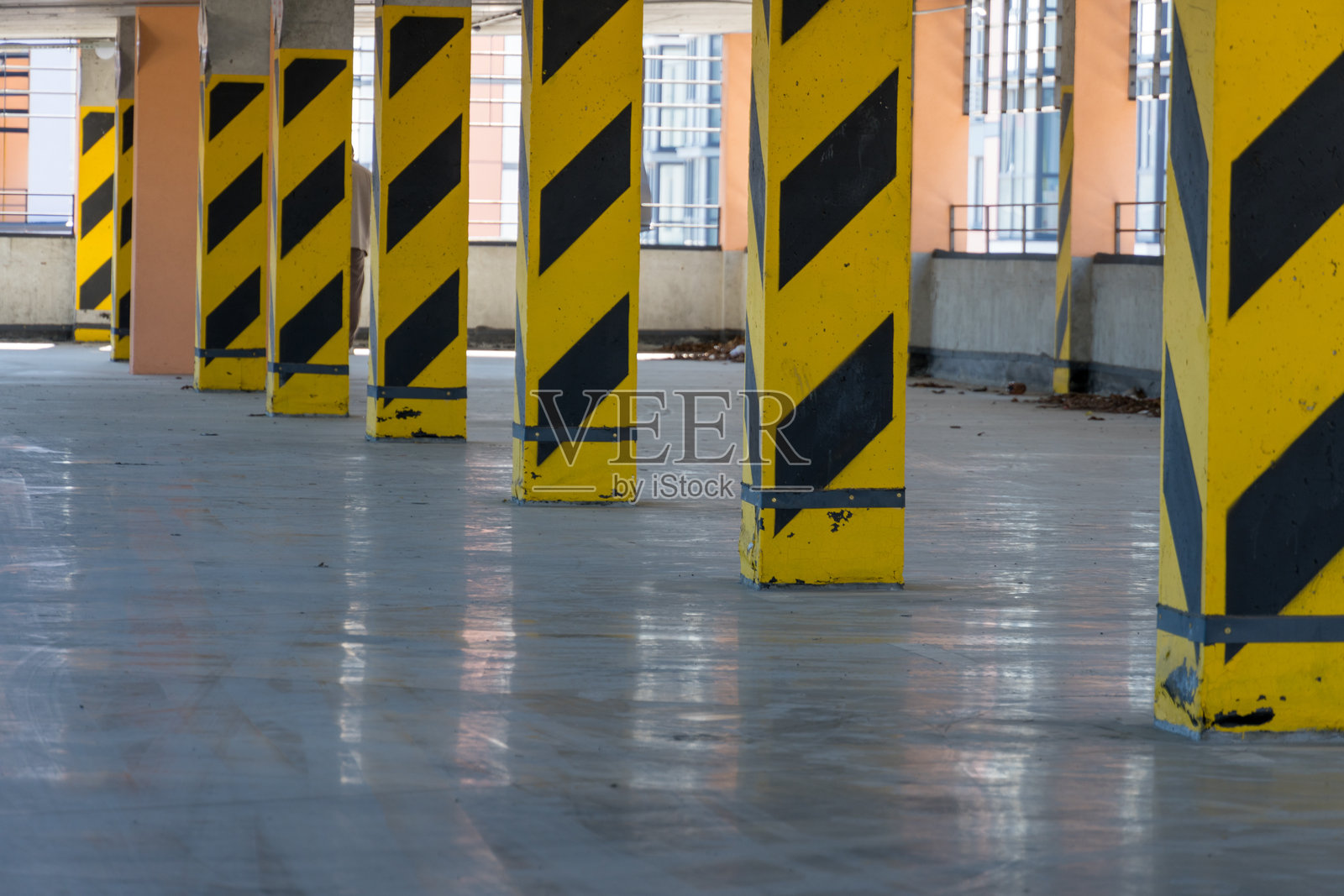 支撑柱设计有黑黄相间的条纹，矗立在宽敞的停车场内。光滑的地面反射出光线，形成鲜明的视觉对比。照片摄影图片